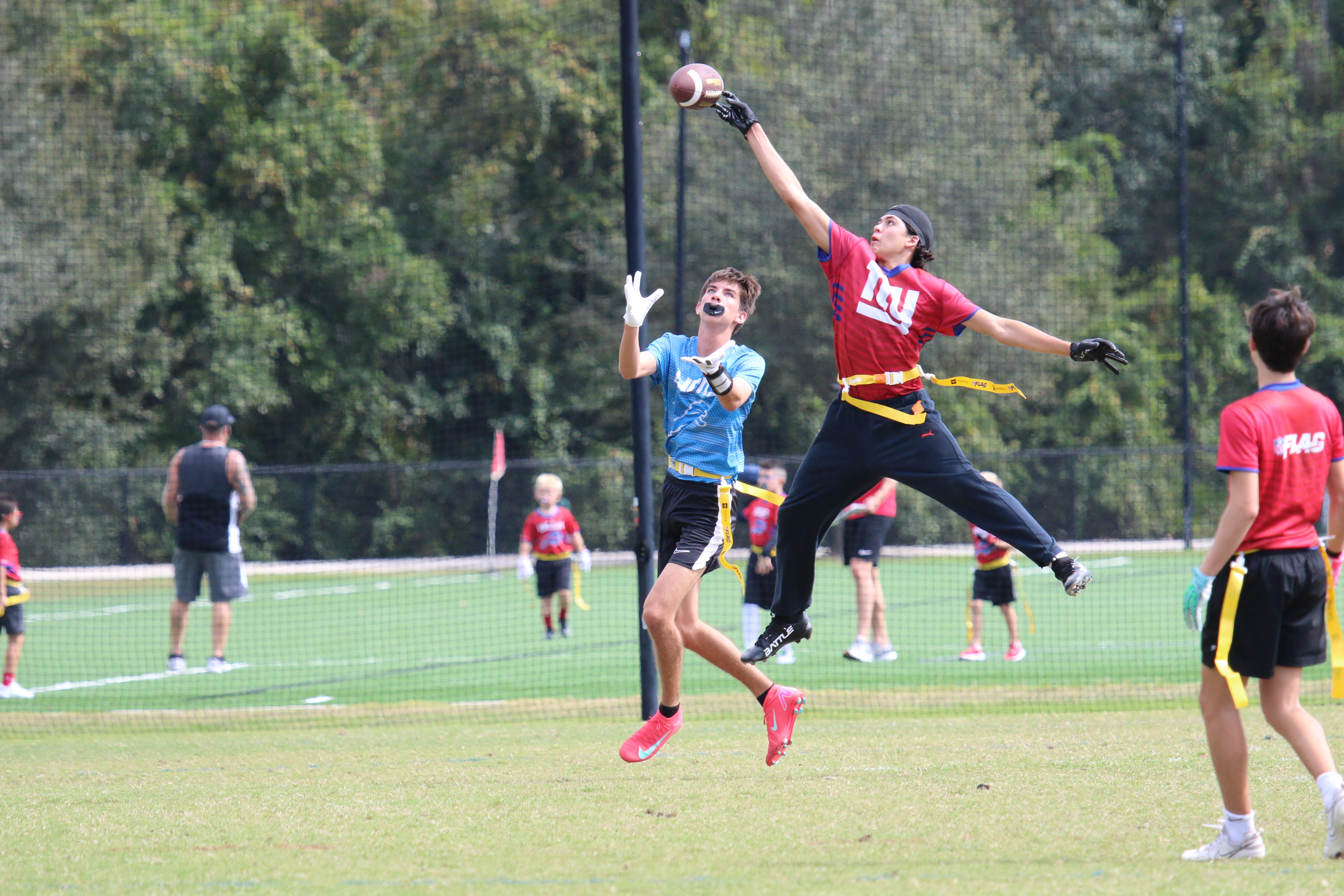 People playing flag football on a grassy field with trees in the background